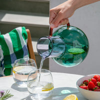 A hand pouring water into a glass from a large teal jug.