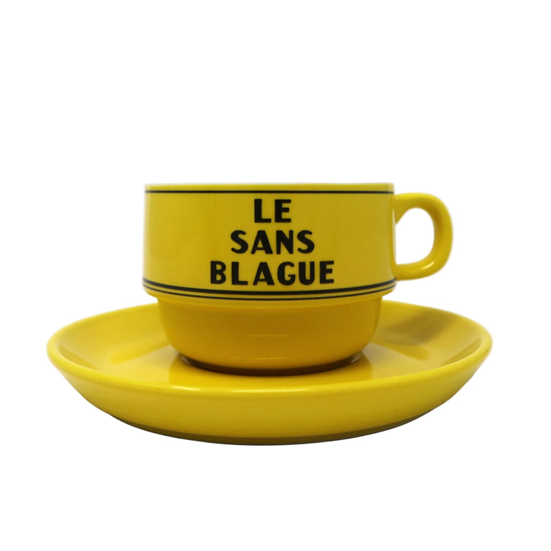 Yellow cup and saucer set with 'LE SANS BLAGUE' text on a white background.