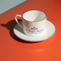 White ceramic cup and saucer with blue text on a red surface.
