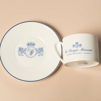 White ceramic mug and saucer with 'The Design Museum' branding on a beige background