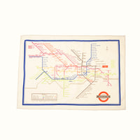 A beige tea towel with a colourful illustration of the London Underground Tube map feauring the London Undergound Transport logo.