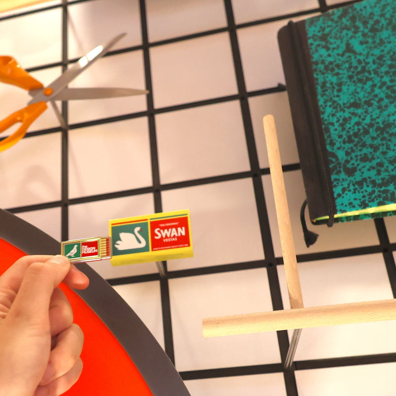 Swan brand matches being held by a hand with scissors and a book in the background.