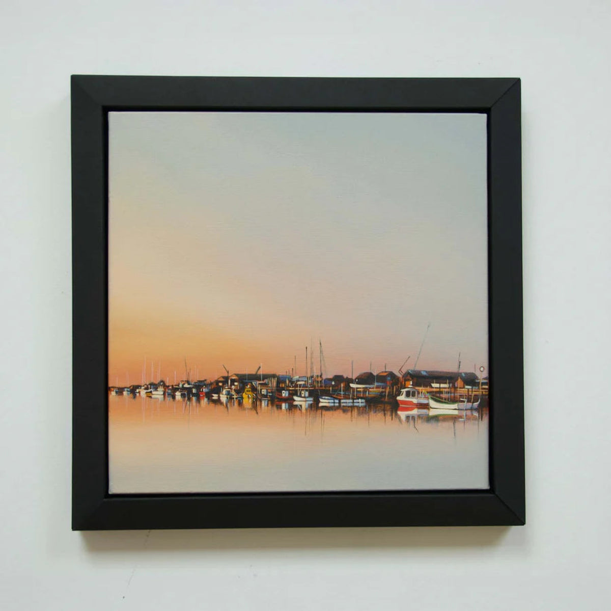 Painting of boats with a sunset in a black picture frame.