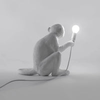 White monkey lamp holding a light bulb on a grey background