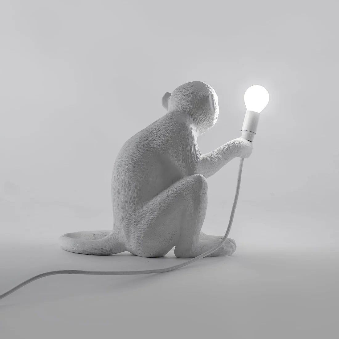 White monkey lamp holding a light bulb on a grey background