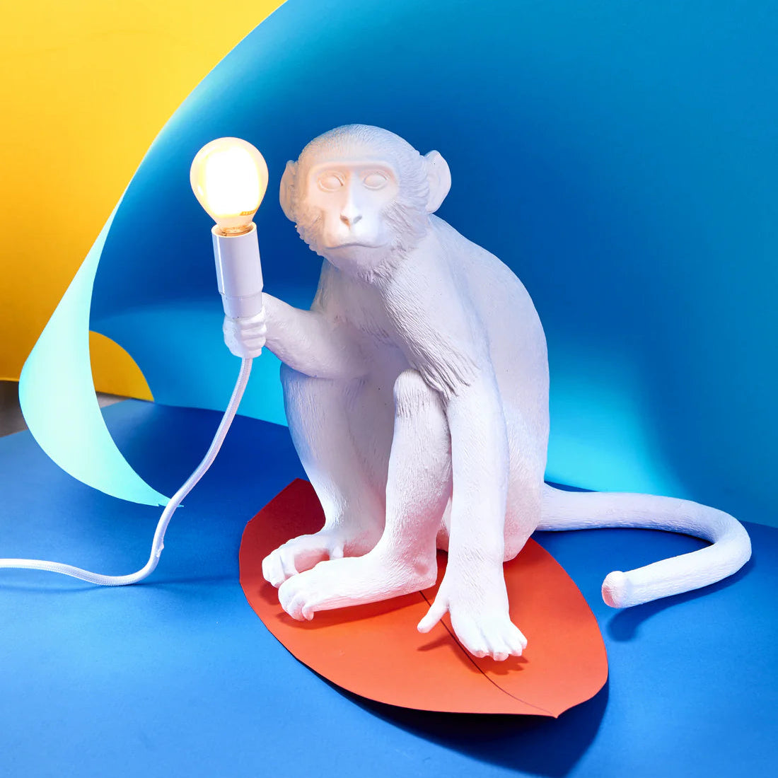 White monkey lamp holding a light bulb on a blue and yellow background