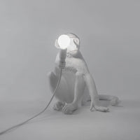 White monkey lamp holding a light bulb on a gray background