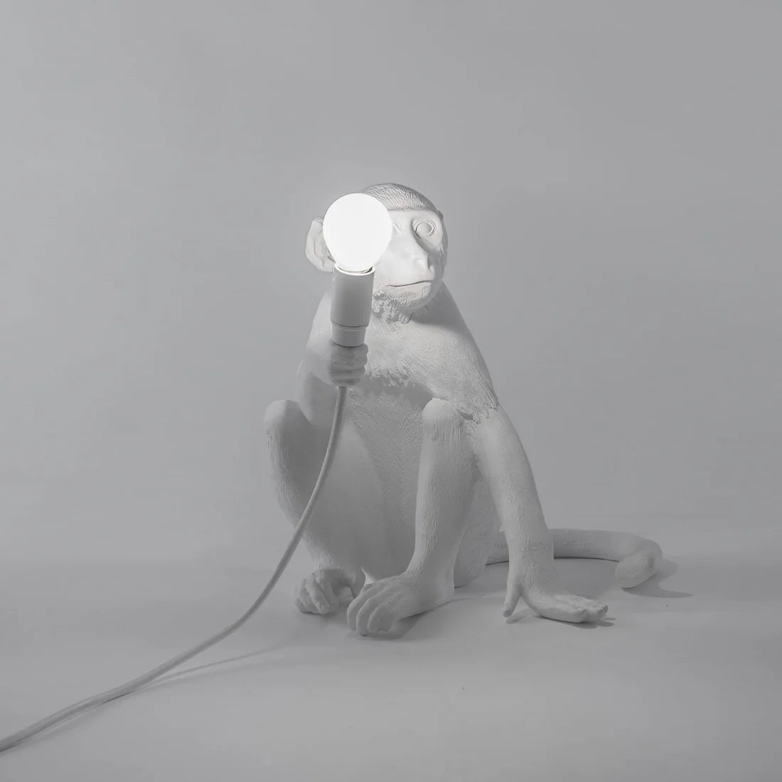 White monkey lamp holding a light bulb on a gray background