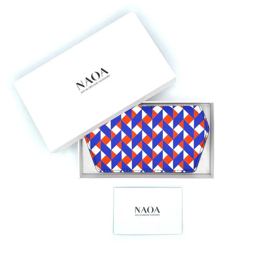 A geometric patterned glasses case in blue, orange, and white, presented in a white tray with its white branded box lid and a small card below. 