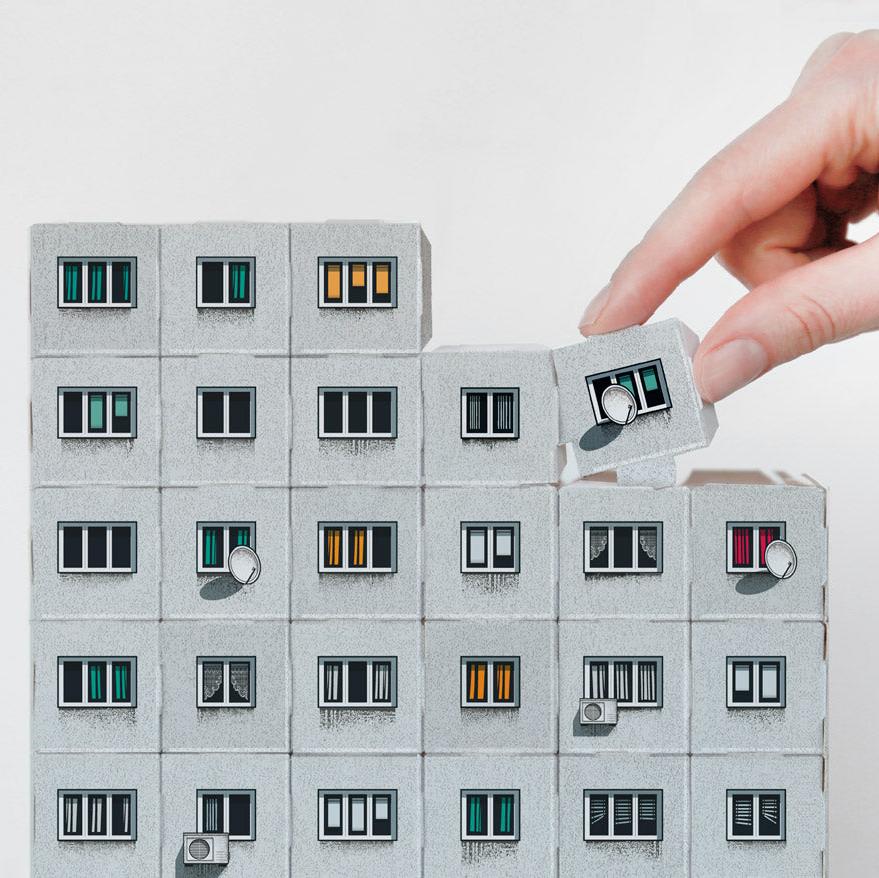 A person's hand putting together a grey paper model of a Brutalist apartment building. 