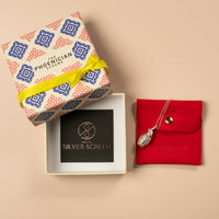 Decorative jewellery box with a yellow ribbon, and a silver grenade necklace on a red pouch against  a beige background