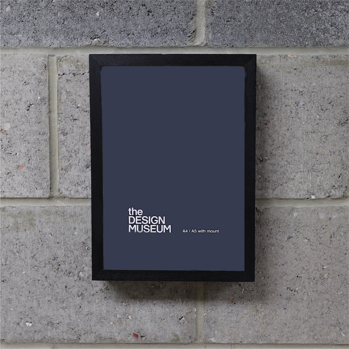 A grey poster in a black picture frame on a brick wall.