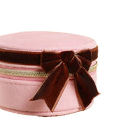 Pink round bag with a brown velvet bow and gold chain on a beige background