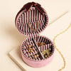 Heart-shaped jewelry box with striped interior, containing gold jewelry on a beige background.