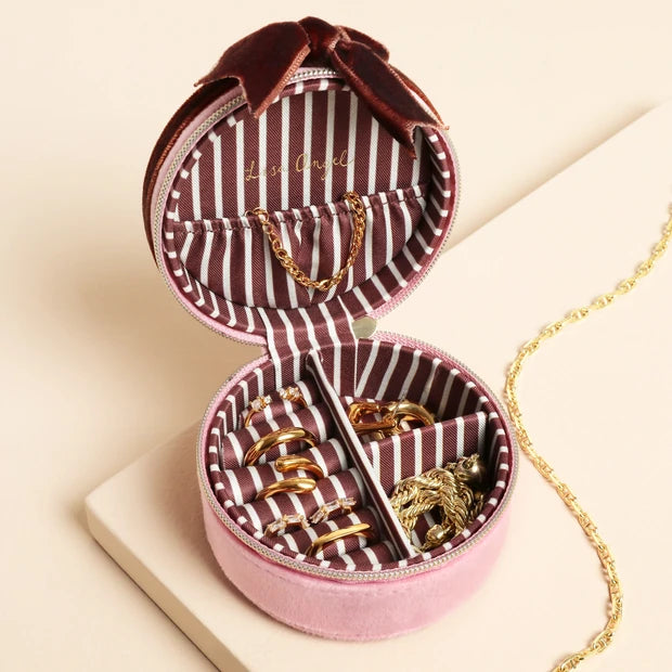 Heart-shaped jewelry box with striped interior, containing gold jewelry on a beige background.