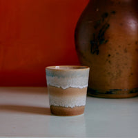 A colourful abstract ceramic mug on a white surface against an orange wall.