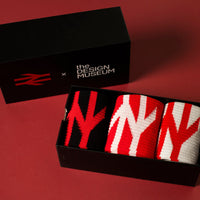 Three pairs of patterned knit socks displayed in an open black box next to a black branded box on a red background. The socks feature large abstract 'N' shapes in red, black, and white.