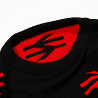 Close-up of a black knit jumper featuring a bold red interior collar with a black stylized logo and red knit details on the lower edge.