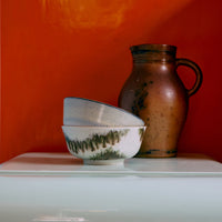 Two green and blue abstract ceramic bowls stacked on white fridge in front of an orange wall.