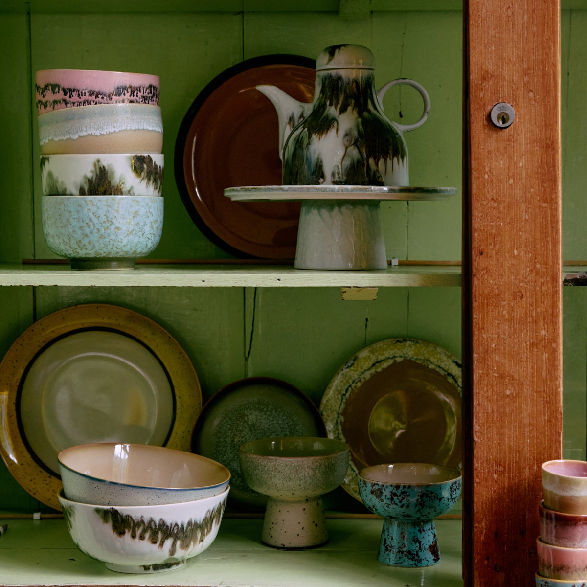 Various colourful abstract ceramics inside a green cupboard.