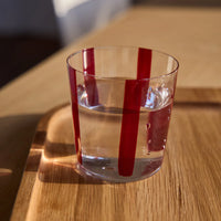 Conran Shop real Christal thin transparent tumbler glass cup with some hand painted burgundy stripes with water on it, lifestyle photo on wood tray, indoors sunny day 