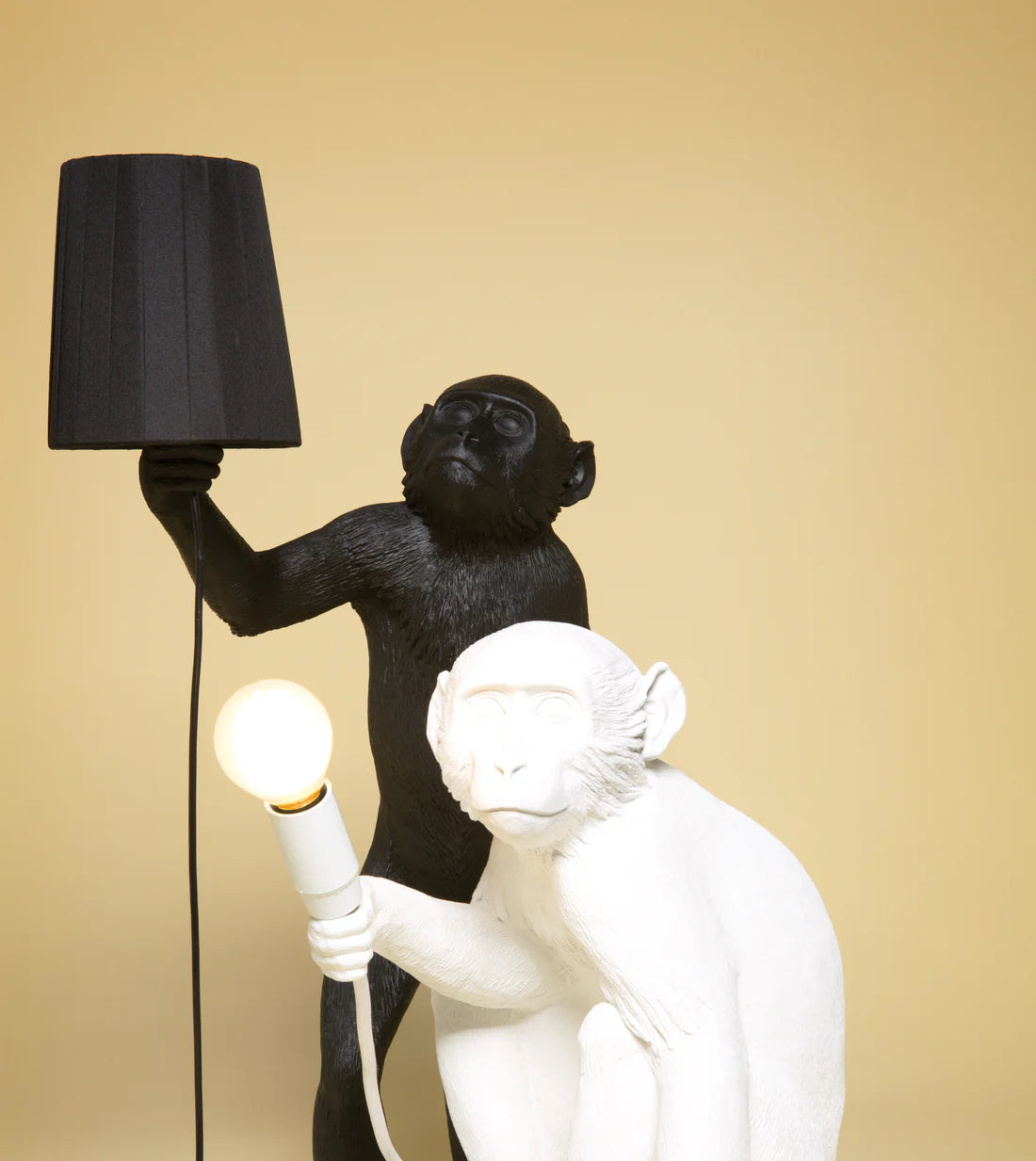 Black and white monkey lamps holding light bulbs against a beige background