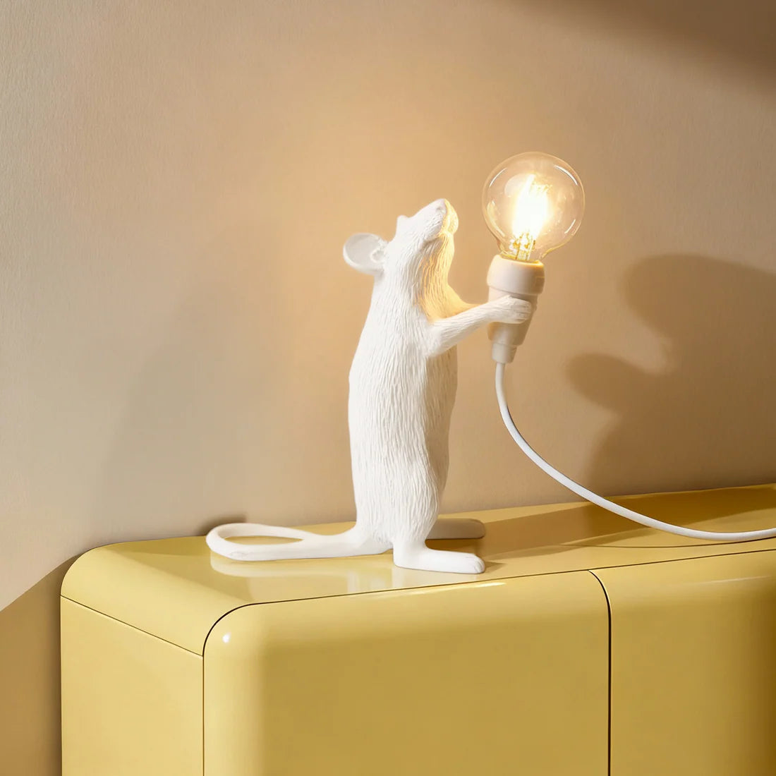 White mouse-shaped lamp holding a light bulb on a yellow surface with a beige wall background