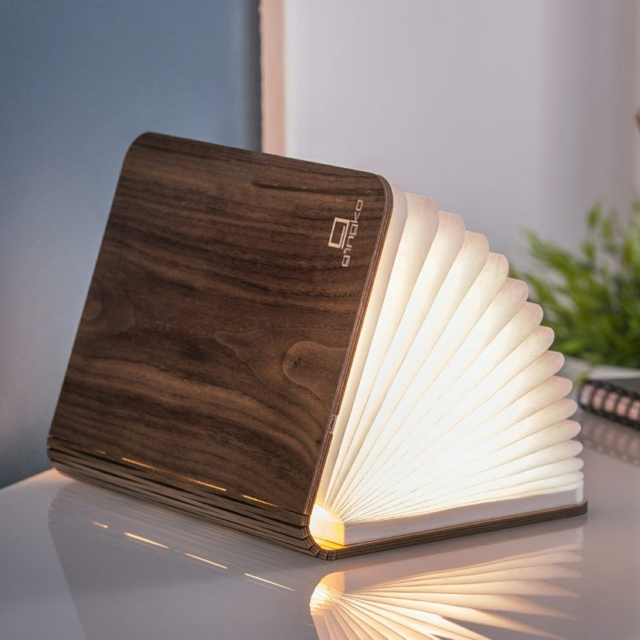 Wooden book-shaped lamp with glowing pages on a reflective surface