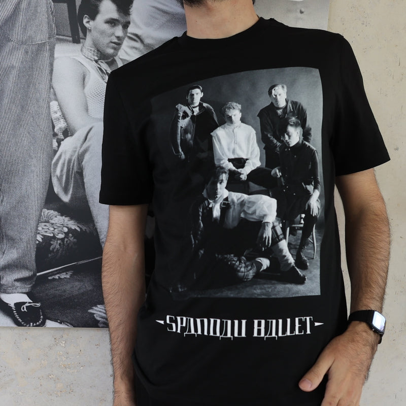 Person wearing a black t-shirt with a graphic design and text, standing against a neutral background.