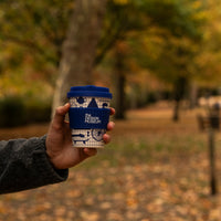 Person holding a blue and white coffee cup with a park background