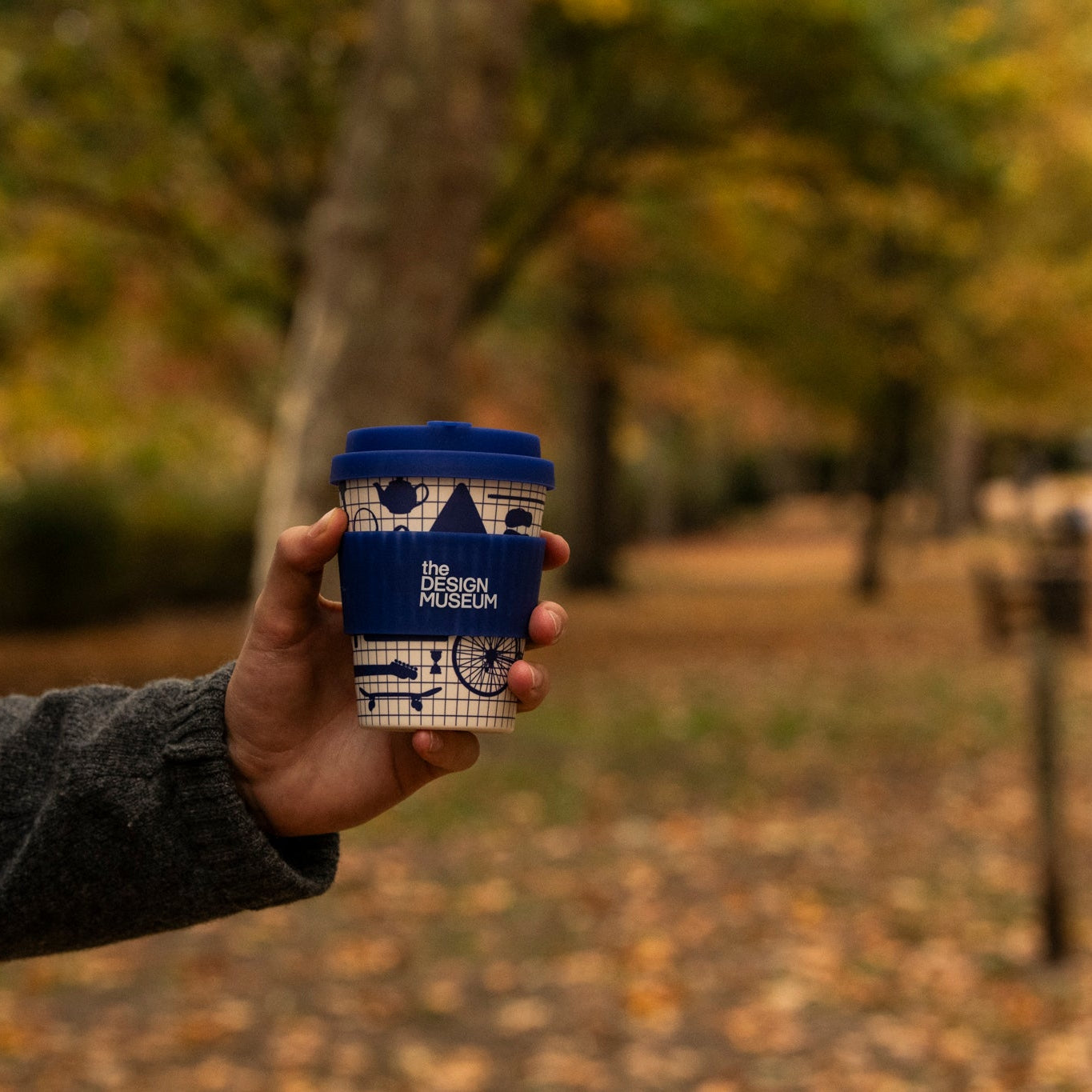 Person holding a blue and white coffee cup with a park background