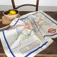 A beige tea towel with a colourful illustration of the London Underground Tube map on a wooden table.