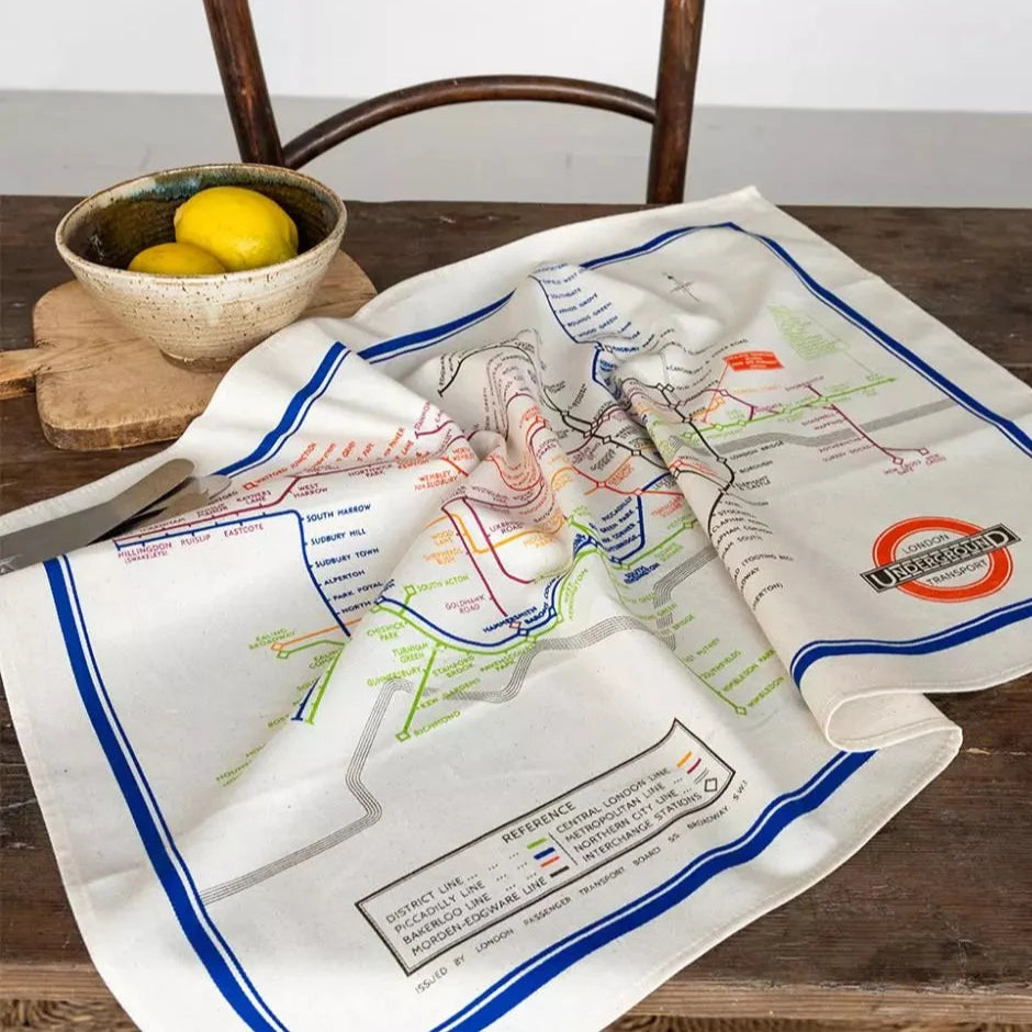 A beige tea towel with a colourful illustration of the London Underground Tube map on a wooden table.