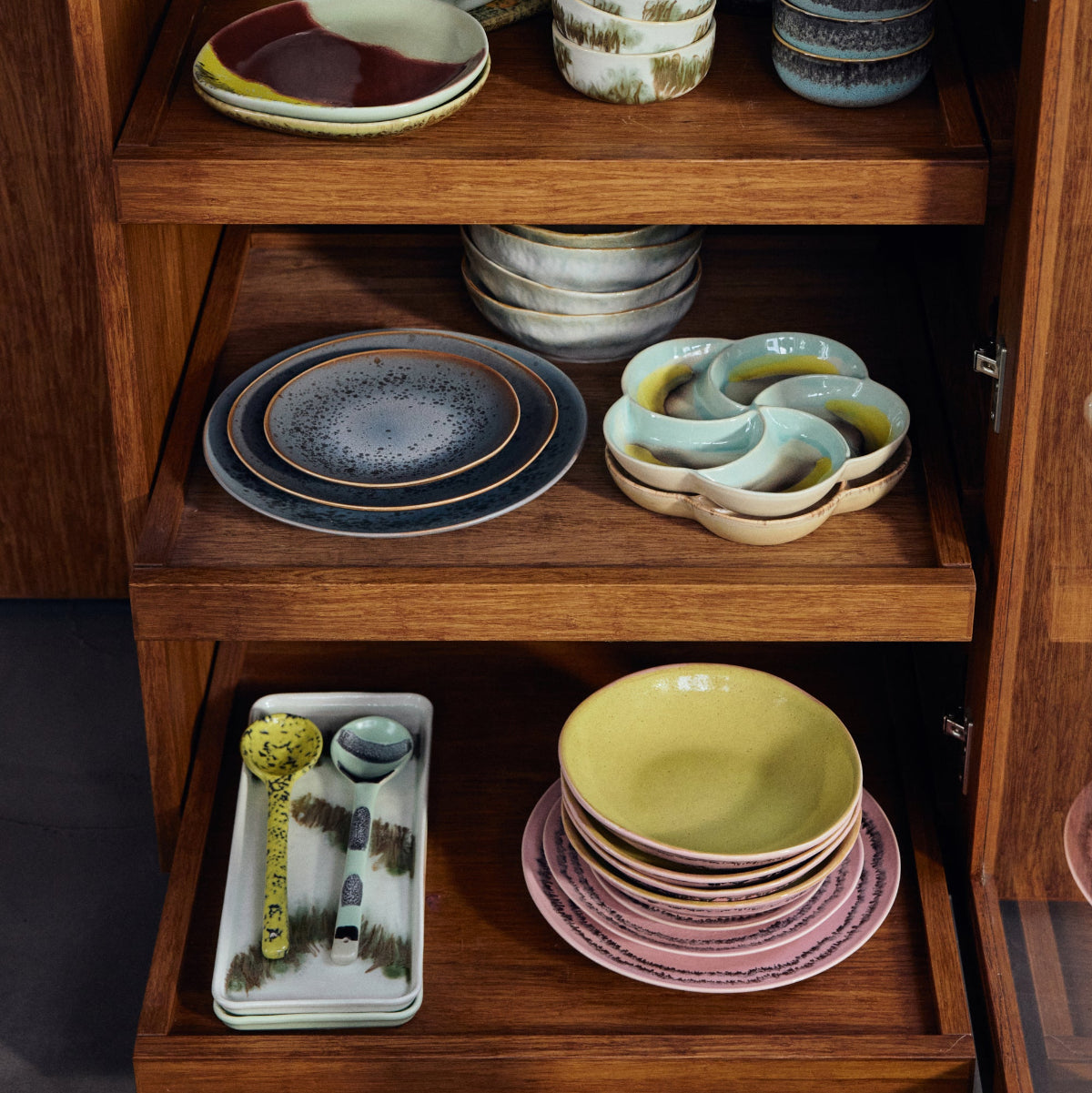 Wooden cabinet with shelves displaying various colourful ceramic dishes and bowls.