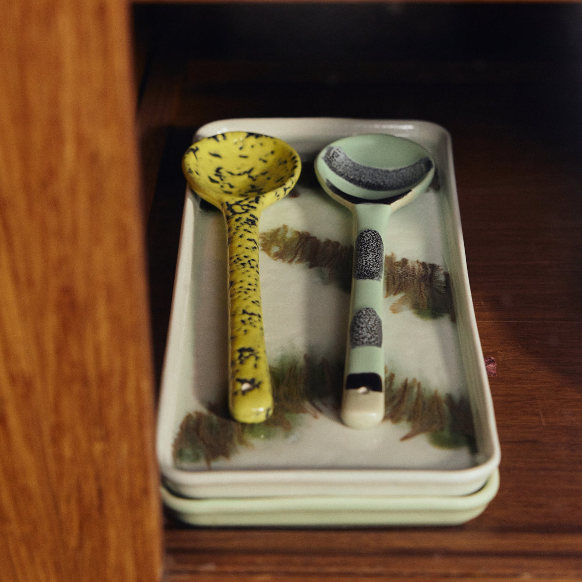Two ceramic ladles on a rectangular tray inside a wooden cabinet