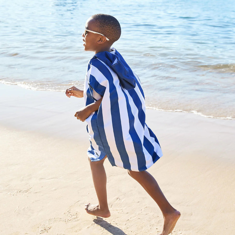 A picture of a child wearing a blue and white striped towelling poncho, running on a beach.