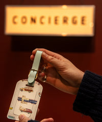 Person holding a luggage tag with a concierge sign and a red wall in the background
