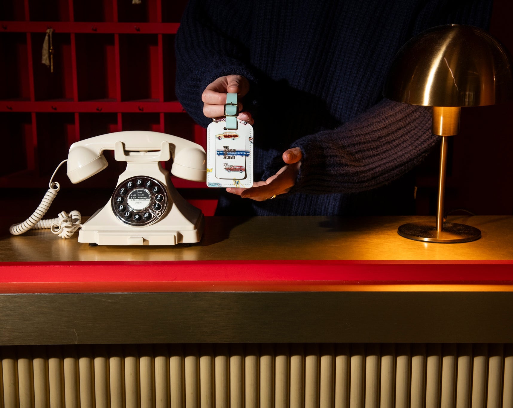 Person holding a white luggage tag next to an old-fashioned telephone on a gold hotel desk.