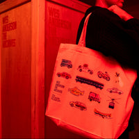 Person holding a tote bag with illustrations in front of a Wes Anderson branded wooden crate in red lighting.