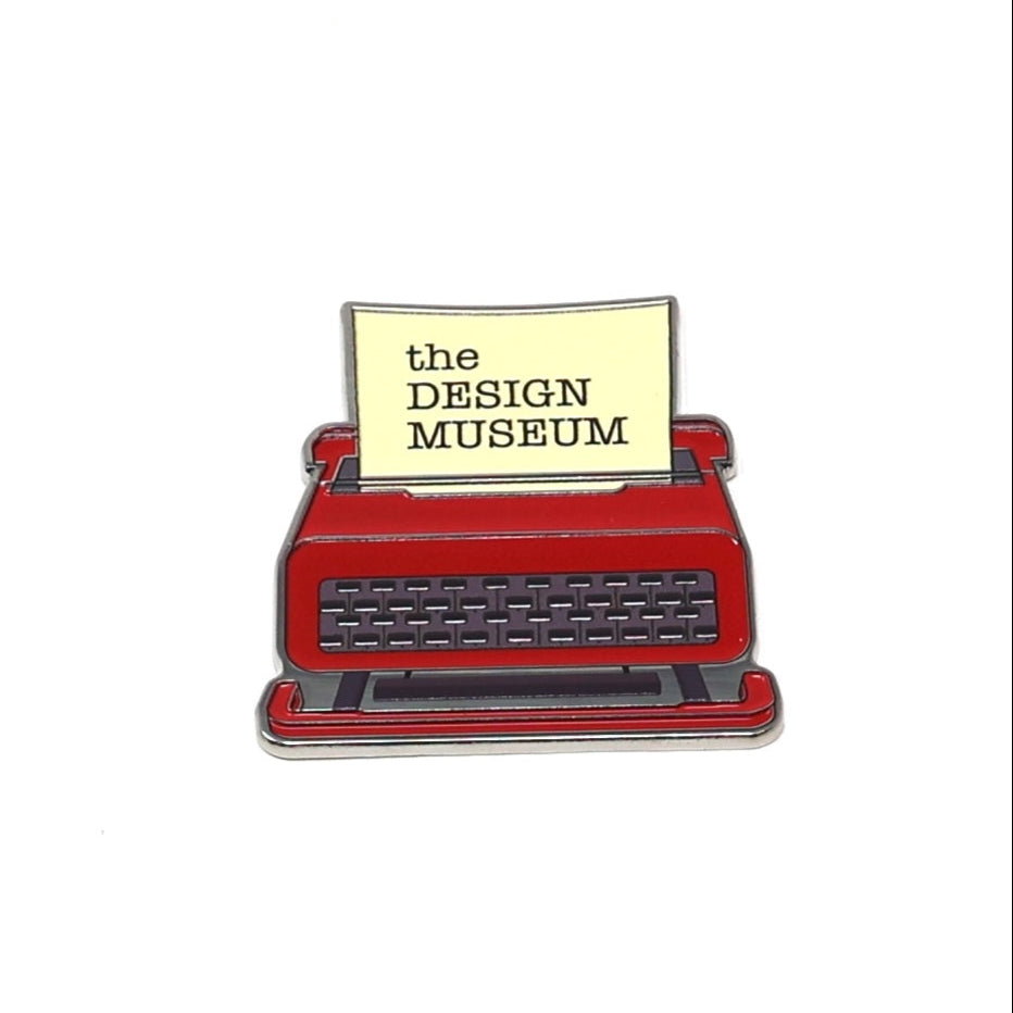 Red typewriter with a yellow sign reading 'the DESIGN MUSEUM' on a white background