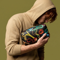 Person holding a black washbag with colourful snake patterns against a green background