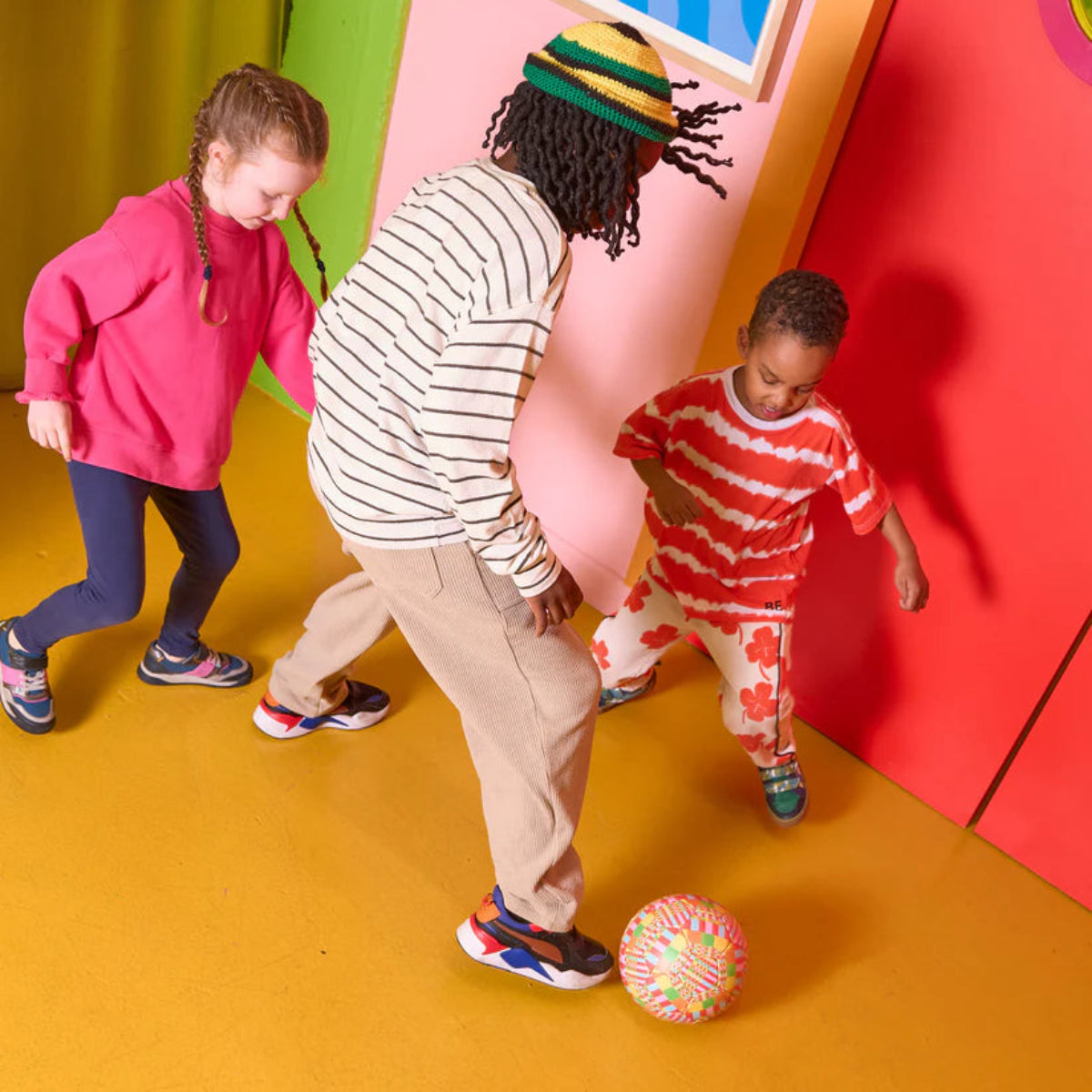 Three children playing with a colourful ball on a vibrant, multicolored floor.