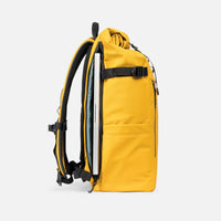 A yellow backpack shown from the side, featuring a zippered pocket, with a silver laptop tucked into its side compartment, against a light gray background.