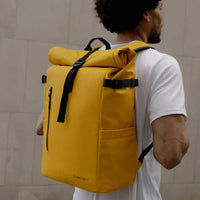 Person wearing a yellow backpack with black straps against a beige wall.