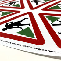 Edge of Margaret Calvert wrapping paper with cartoon person holding a christmas tree inside a red triangle.