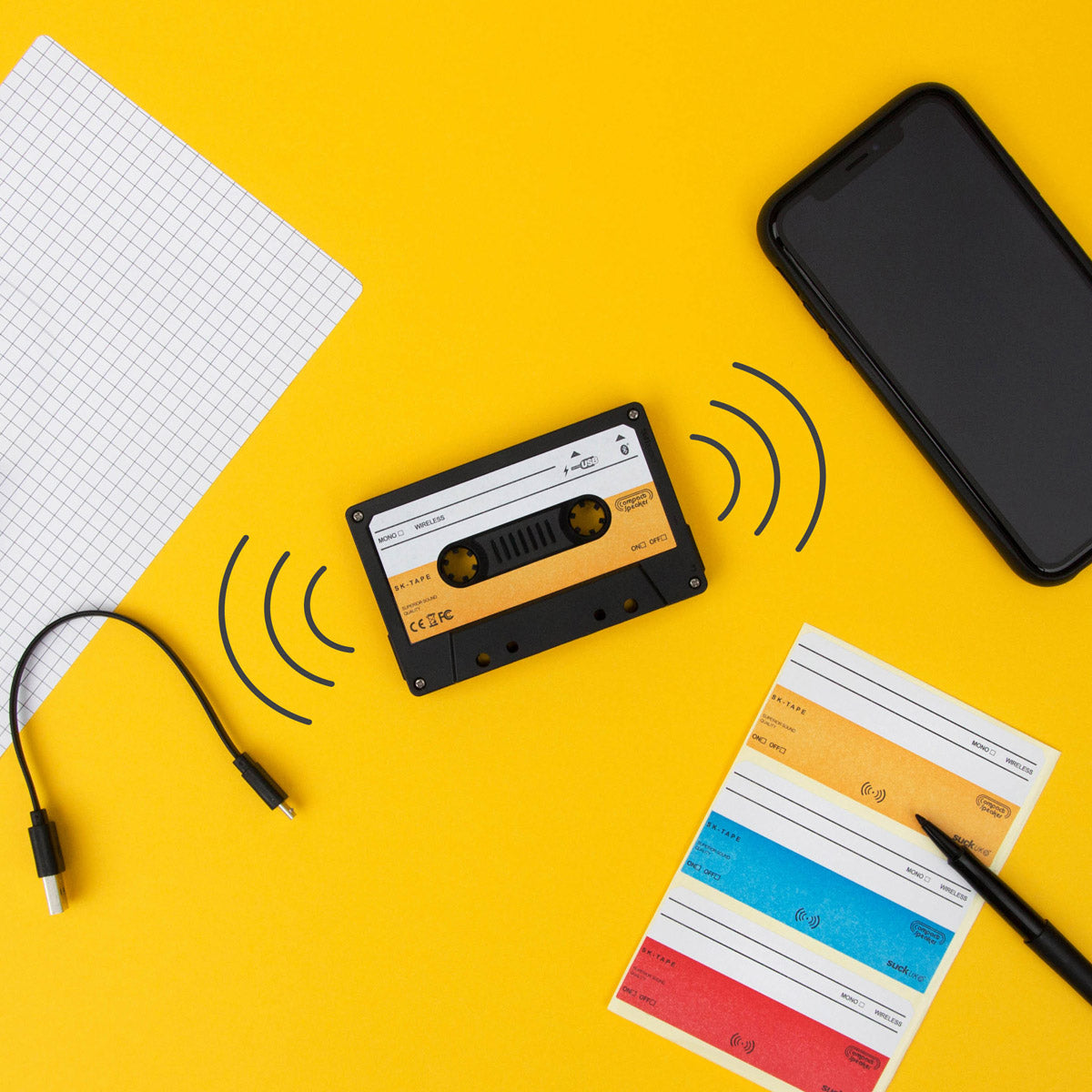 Wireless cassette speaker with colourful stickers and phone on a yellow background