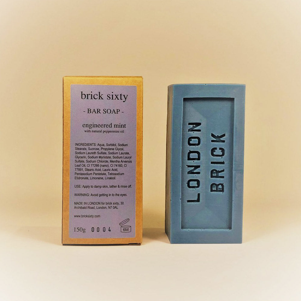 Grey rectangle bar of Engineered Mint soap and brown and grey packaging on a light yellow background